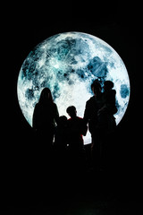 Silhouette picture of a family stands on the mountain with A big full moon at night.