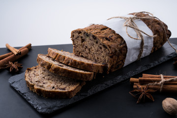 Sliced vegan homemade  banana bread with nuts and berry in the baking paper on the wooden table, selective focus.  cinnamon, anis stars around.
