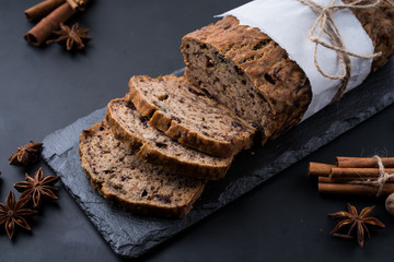 Sliced vegan homemade  banana bread with nuts and berry in the baking paper on the wooden table, selective focus.  cinnamon, anis stars around.