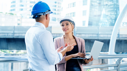 Business engineer Men and women standing and talking meeting is on job site. Wear blue and white helmet for safety. Use the laptop to enter into an agreement to participate in construction business