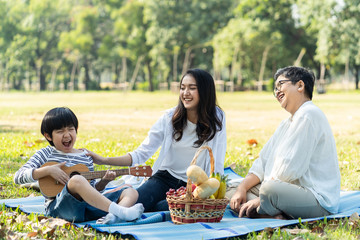 Asian family having picnic in fresh green park together. Mother touching to kid with smile while...