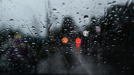 Blurry cars and lights in traffic. Rain drops on windshield glass window