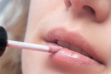 girl paints her lips with lip gloss. Photo close-up