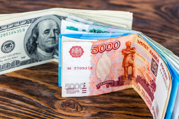 a two bunches of russian rubl and us dollar banknotes standing on brown wood surface close-up with...