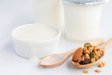 Healthy flavored yogurt in plastic cup and ceramic bowl with granola in wooden spoon on white background. With copy space for text.