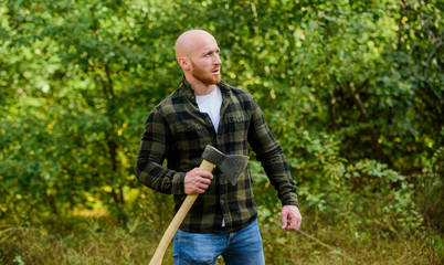 man checkered shirt use axe. brutal and attractive male in forest. power and strength. lumberjack carry ax. bald woodsman worker. live on rancho. concept of masculinity. bearded hipster cut tree