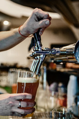 Fototapeta na wymiar bartender hand at beer tap pouring a draught beer in glass serving in a restaurant or pub