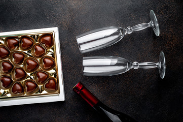 Candy in the form of a heart in a box, a bottle of wine or champagne and two glasses for Valentine's Day on a stone background with copy space for your text. Valentine's Day celebration concept.