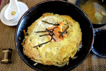 A black bowl of Katsudon menu,a famous Japanese food on wooden dinning table