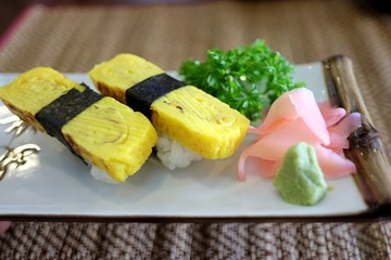 Japanese Tamago egg sushi in a white plate with parsley and pickled ginger on dinning table top view
