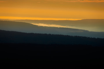 Gently undulating forest landscape in the Harz Mountains at sunrise with glowing sky and black forest