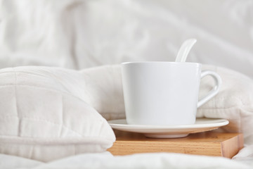 Cup of coffee on white bed on wooden stand. Close up.
