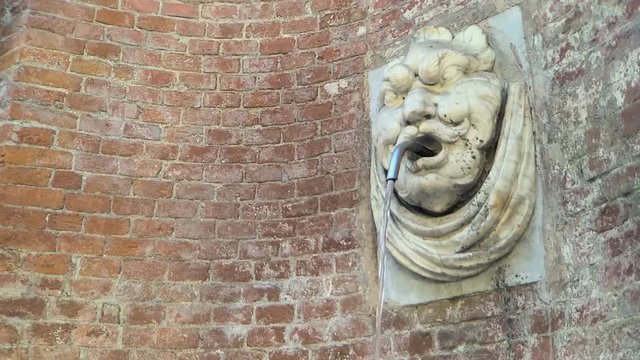 Marble fountain with demon face on brick wall