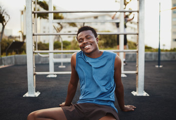 Portrait of a smiling young african american male athlete relaxing after intense workout in the outdoor gym park