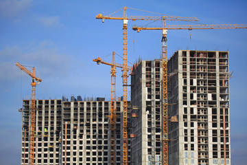 High-rise construction cranes and array of buildings under construction on the blue sky background. Building construction site with cranes. The construction of modern apartment buildings estate