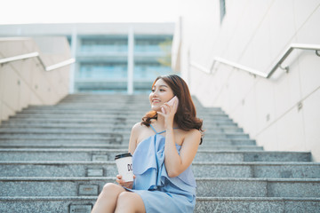 Cheerful young Asian girl talking on phone while sitting at outdoor stair. Lifestyle of urban girl.