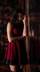 Pretty young sexy model female with dark hair in amazing long red dress and black shoes posing in dark studio