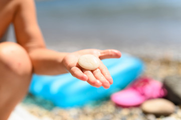 round white sea stone in a child's hand on the background of the beach