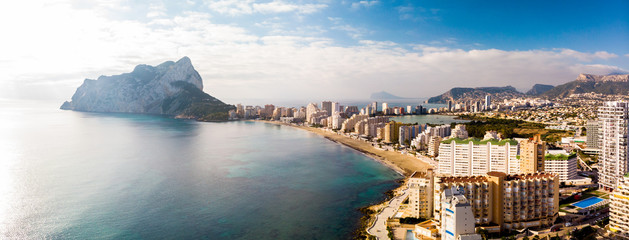 Aerial view of Calpe city in Alicante, Spain, at sunrise. La Fossa beach is in the foreground and de Ifach Penon rock in the background. - obrazy, fototapety, plakaty