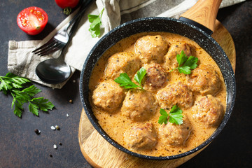 Meatballs in sour cream and tomato sauce in a pan on a dark stone or slate table. Copy space.