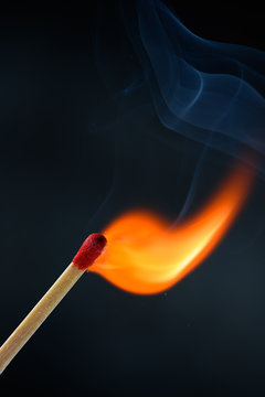 Wooden match stick with red head ignited and burning bright big fire flame with smoke on black background.