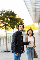 Fototapeta premium Happy to be together. Beautiful young couple holding hands and looking at each other with smile while walking through the city street