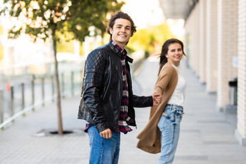 Happy to be together. Beautiful young couple holding hands and looking at each other with smile while walking through the city street