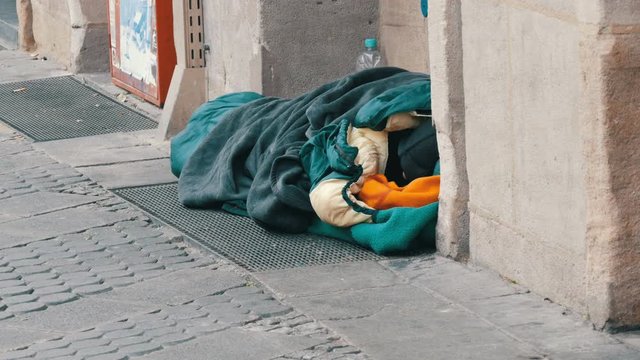 Nuremberg, Germany - December 10, 2019: A homeless poor beggar lying on the ground in a sleeping bag and asks for alms on a city street in winter