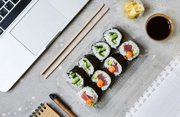 Food delivery. lunch box with sushi roll with tuna, avocado, cucumber and soy sauce on a gray office desk. takeaway lunch at the office. sushi menu delivery. Selective focus