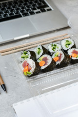 Food delivery. lunch box with sushi roll with tuna, avocado, cucumber and soy sauce on a gray office desk. takeaway lunch at the office. sushi menu delivery. Selective focus