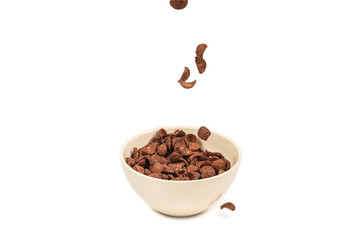 Chocolate corn flakes falling to the white bowl isolated on white. Motion.