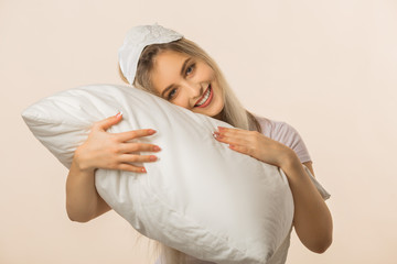 beautiful young woman in a sleep mask on a beige background with a pillow in her hands