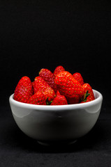 Fresh strawberry in white bowl on black background