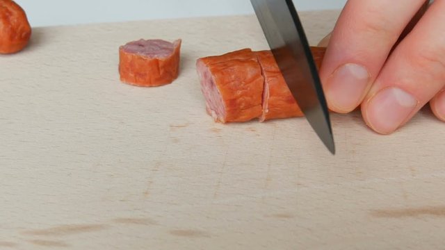 Female hands cut slice hunting sausage on a wooden kitchen board with a black ceramic knife