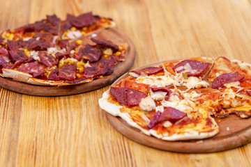 Pizza on wooden platter. Burnt pizza. Junk food, fat, unhealthy eating, bad habits. Fresh italian pizza with salami, tomato and cheese served on. Italian traditional meal