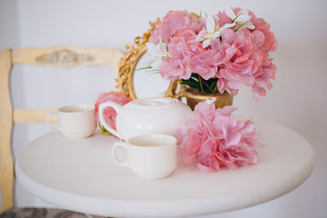 Tea table, mugs and a teapot white teapot with a pink bouquet of flowers in the rococo style. Golden vintage mirror. White pink eltion interior