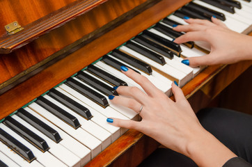 Fototapeta premium hands of a female pianist with blue nail Polish on the nails on the keys of a piano. girl playing the piano.