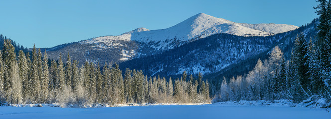 Panoramic view of a mountain valley. Winter forest, snow-capped mountain peaks. Wild place in Siberia.