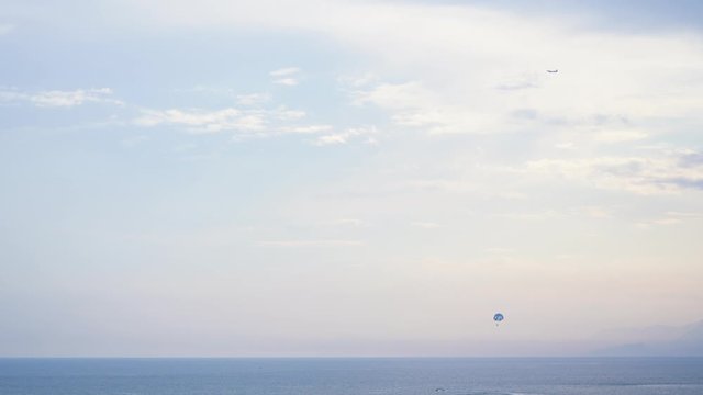 Different kinds of transport in blue sea and sky. Plane flying in heaven, and tourists enjoying water sport flying with parachute pulled by motorboat. Real time 4k video footage.