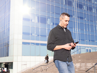 Handsome middle aged business man walking in modern city street, using his phone handsfree, daylight