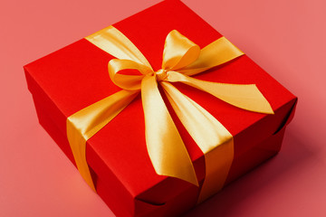 red box tied with a gold ribbon. the ribbon is tied on a box in the form of a beautiful bow. holiday gift concept