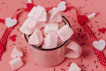 pink mug on a pink background filled with marshmallows in the form of hearts. valentine's day holiday concept