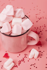 pink mug on a pink background filled with marshmallows in the form of hearts. valentine's day holiday concept