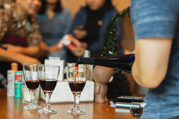 Hand pouring red wine in glass during party with friends.