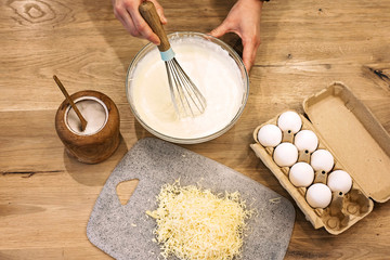 The hands of a professional chef prepare a whisk for pouring quiche loren pie from cream of egg...