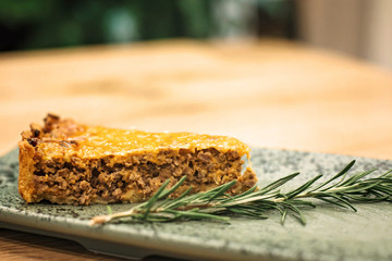 A piece of delicious meat pie with crispy cheese crust on a plate in a section.