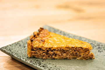 A piece of delicious meat pie with crispy cheese crust on a plate in a section.