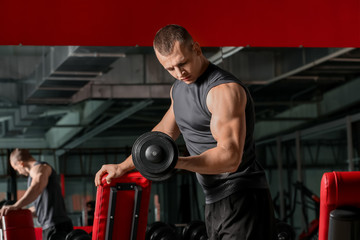 Fototapeta na wymiar Sporty muscular man training with dumbbells in gym