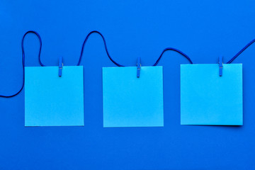 String with blank paper sheets and pegs on blue background