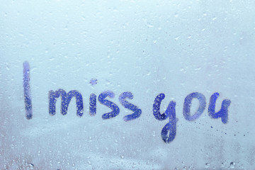 Foggy glass on window with written finger word blue color I miss you concept of loneliness, sadness photo with copy space on blue background